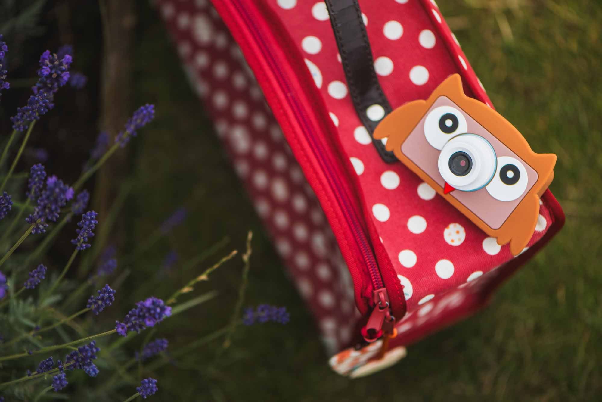 blue digital kids camera with owl sleeve, camera is lying on red suitcase in garden