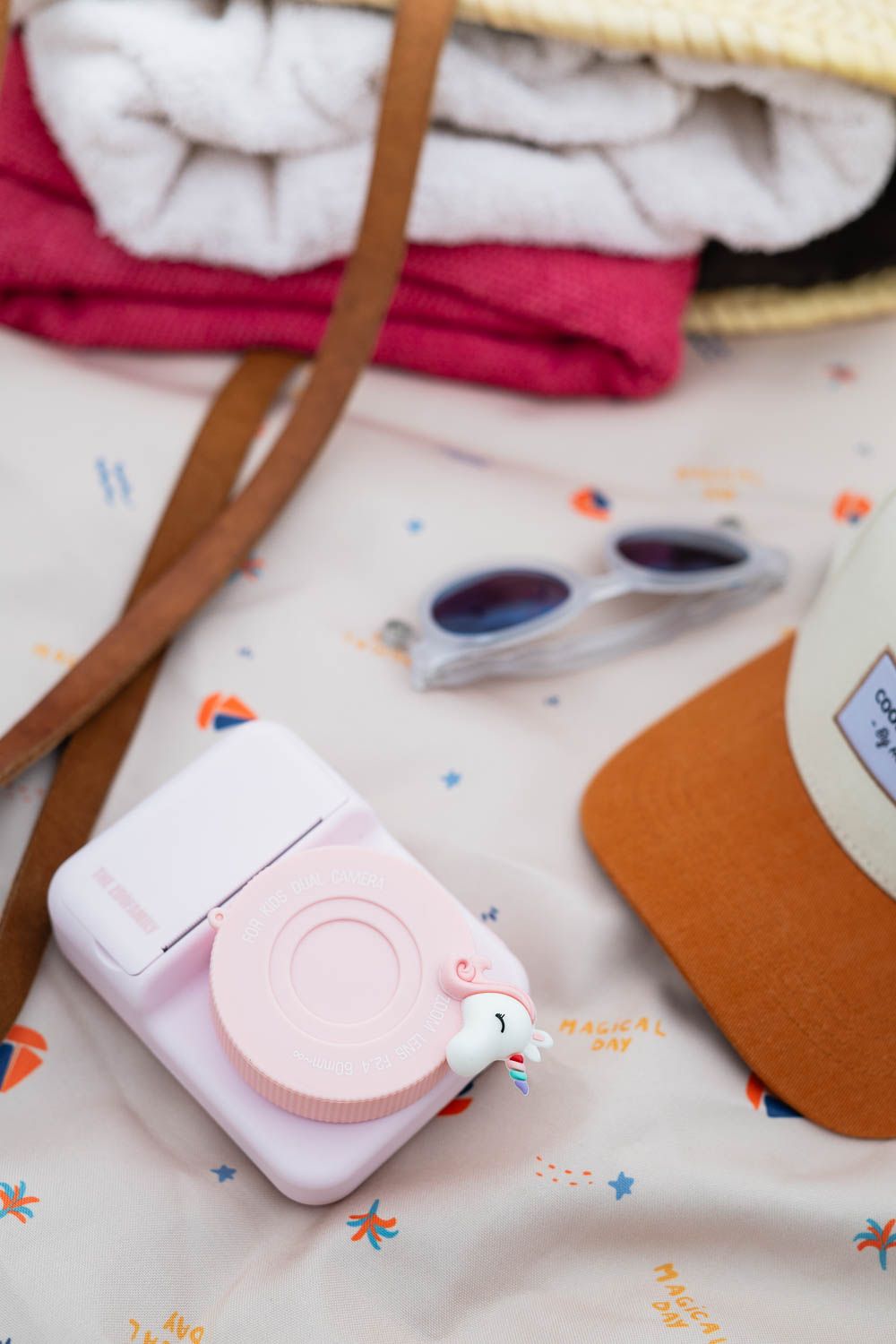 zoo print unicorn digital kids camera, laying on an outdoor beach bag of Play&Go, hat, towels and sunglasses
