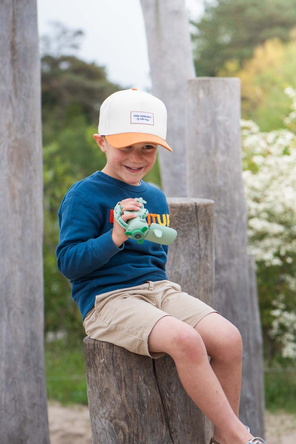 zoo video dino green digital kids camera, child is sitting on a tree trunk, laughing and holding the video camera in its hand