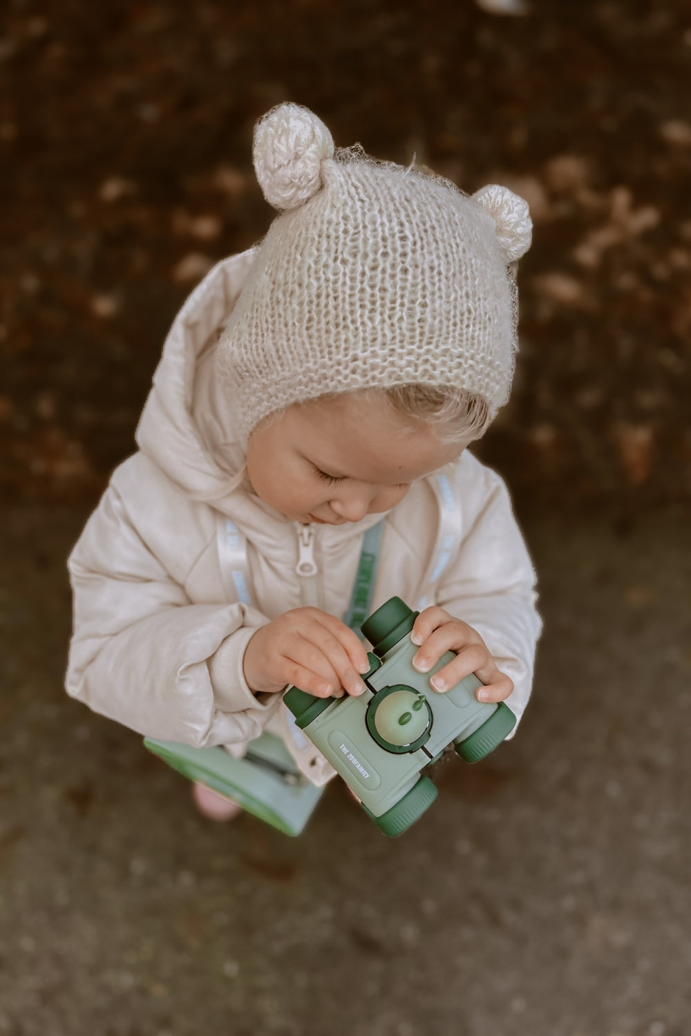 The girl is looking closely at the binoculars.
