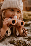 odalA girl is lying and smiling on the ground, holding the binoculars.