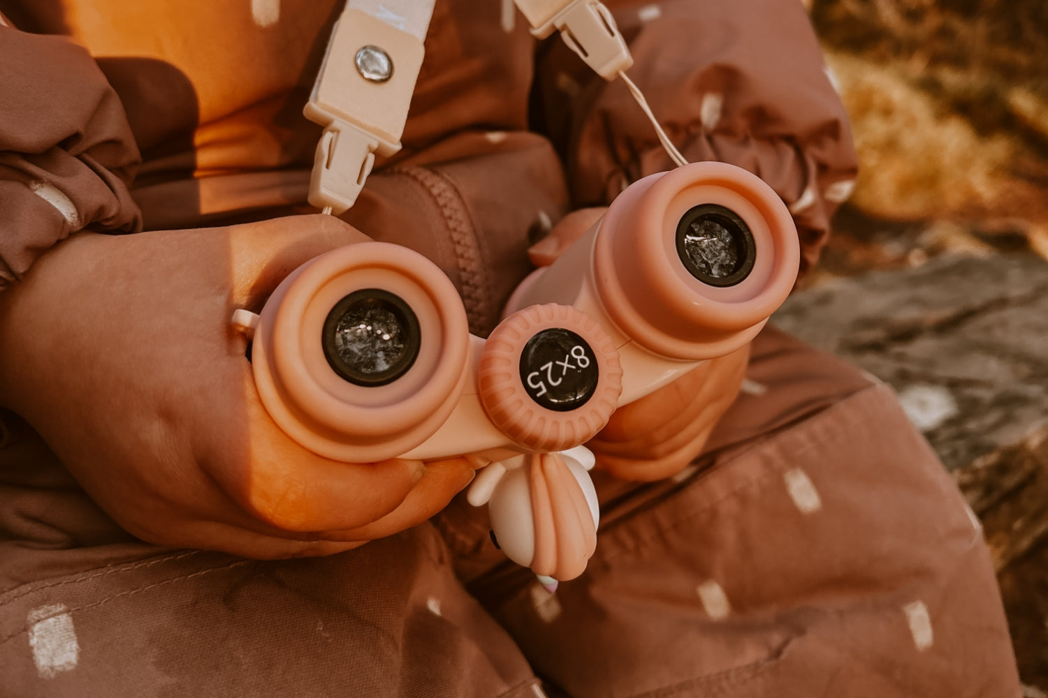 The binoculars are hanging around the girl's neck, and she is holding them in her hands.
