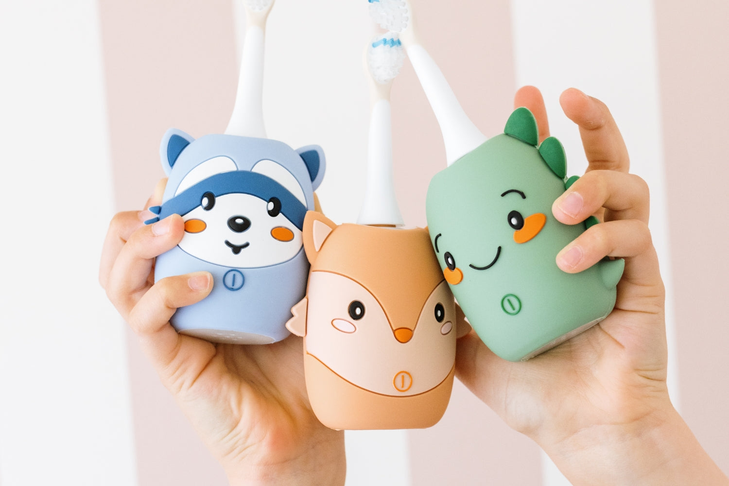 Three toothbrush are shaped like a raccoon, fox, and dinosaur.