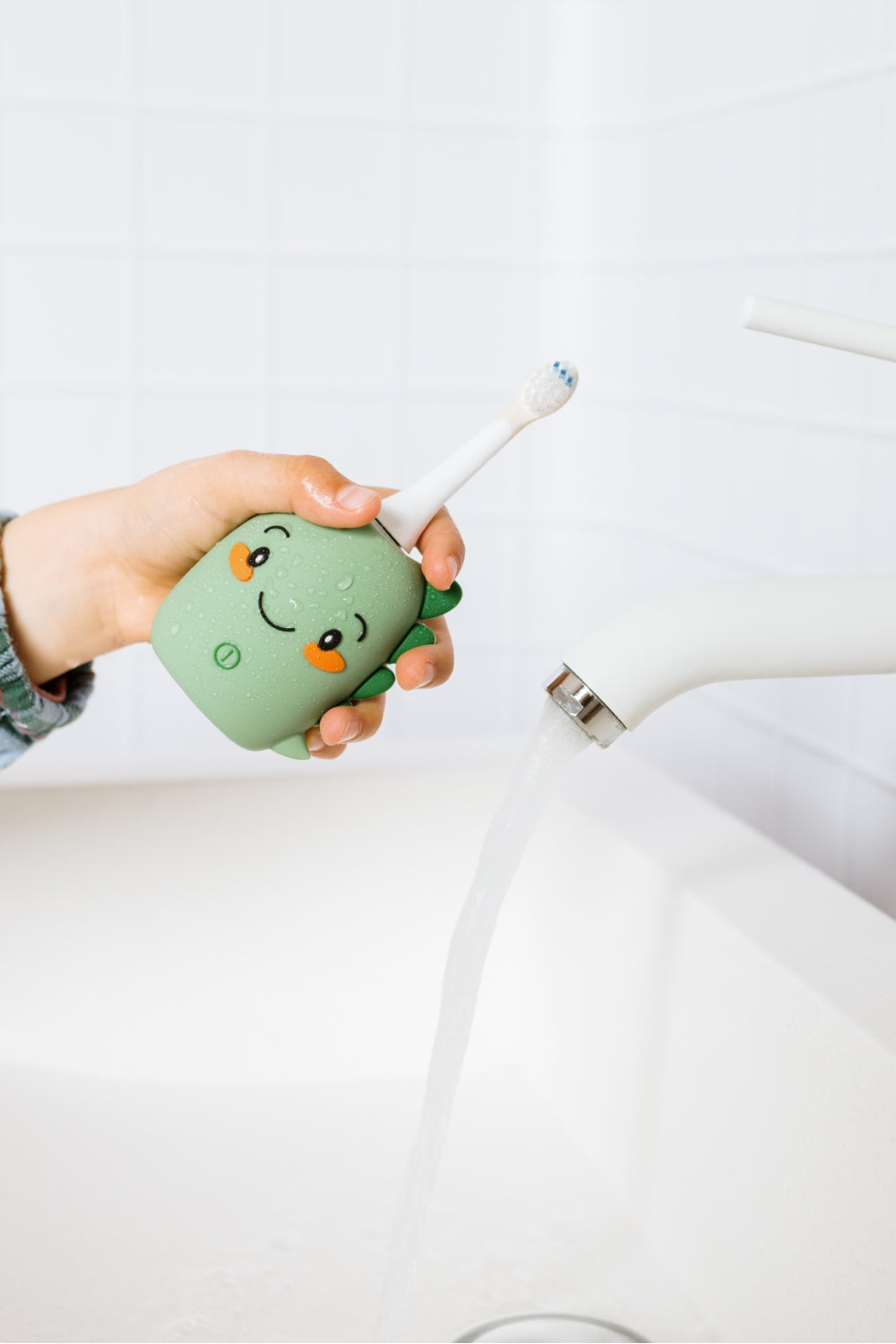 A hand holds a white electric toothbrush dino