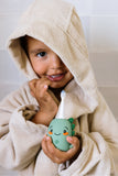 odalA smiling child wrapped in a beige hooded towel holds dino green toothbrush