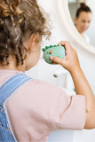 odalA child with curly brown hair uses a dino toothbrush while looking into a bathroom mirror.