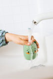 odalA dino toothbrush  with running water from a faucet in a white sink. A child's hand are visible holding the product.
