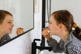 odalA happy girl brushing her teeth with the Fox toothbrush while looking at herself in the mirror.