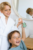 odalTwo children in white and blue bathrobes smiling in a bright bathroom, holding a small fox and dino toothbrush and its matching holder.