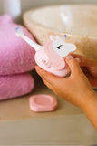 odalA pink and white unicorn-shaped electric toothbrush being held by hands 