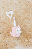 odalA pink unicorn-shaped toothbrush and a white heart-shaped hook, displayed on a textured beige stone surface.