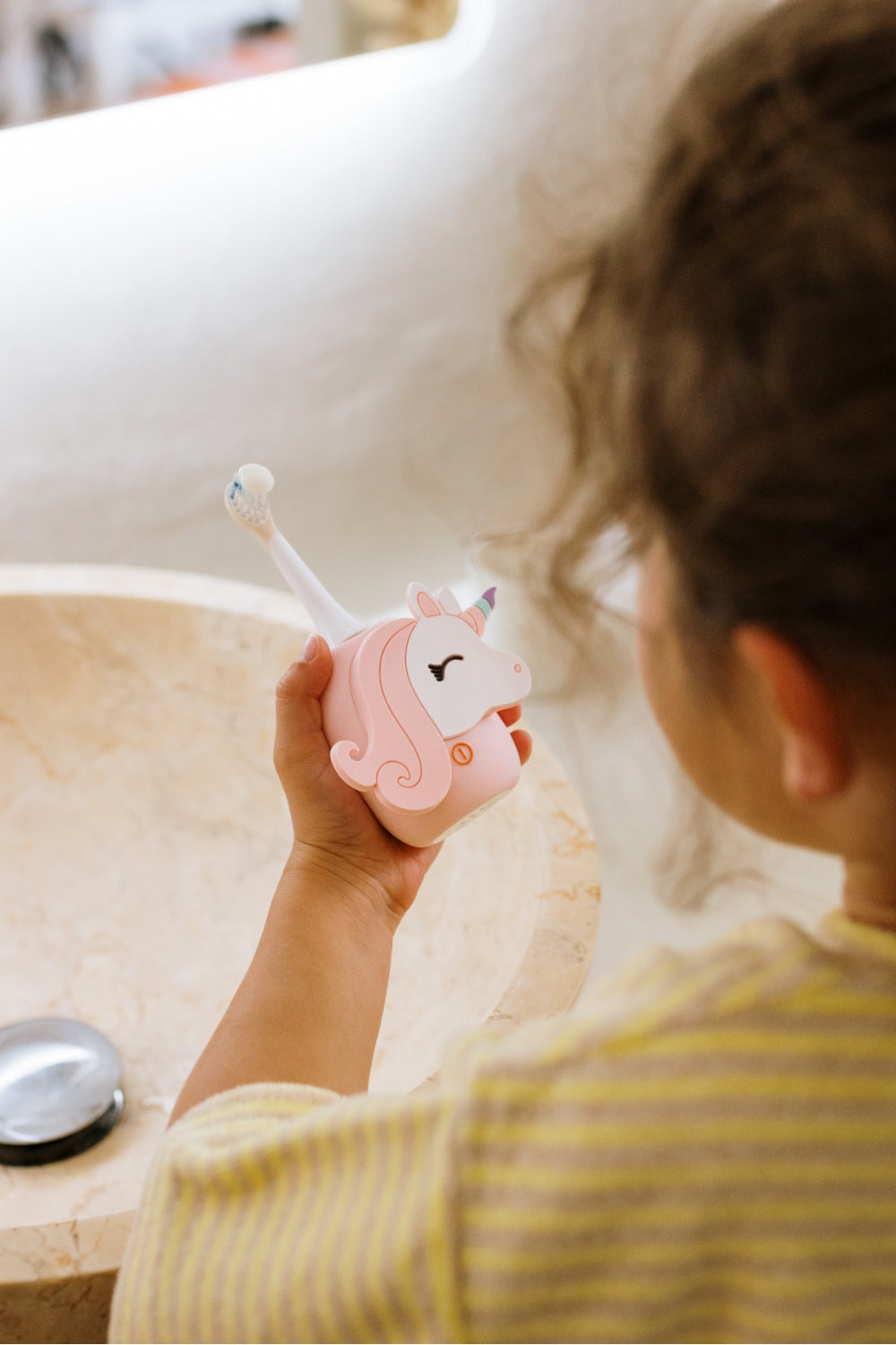 A child holds a pink unicorn-shaped toothbrush