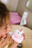 odalA young child using a small pink unicorn-shaped toothbrush in a bathroom setting.