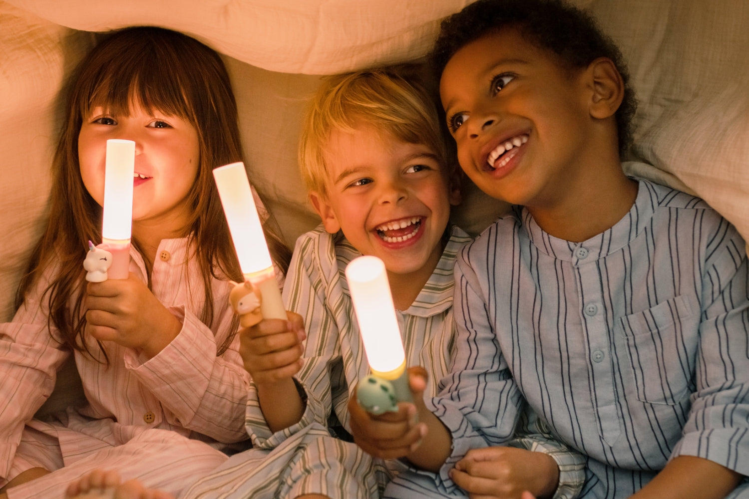 Three children holding Zoo Light lamps under a blanket.