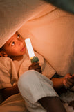 odalA child holding a glowing Zoo Light Dino lamp under a blanket.