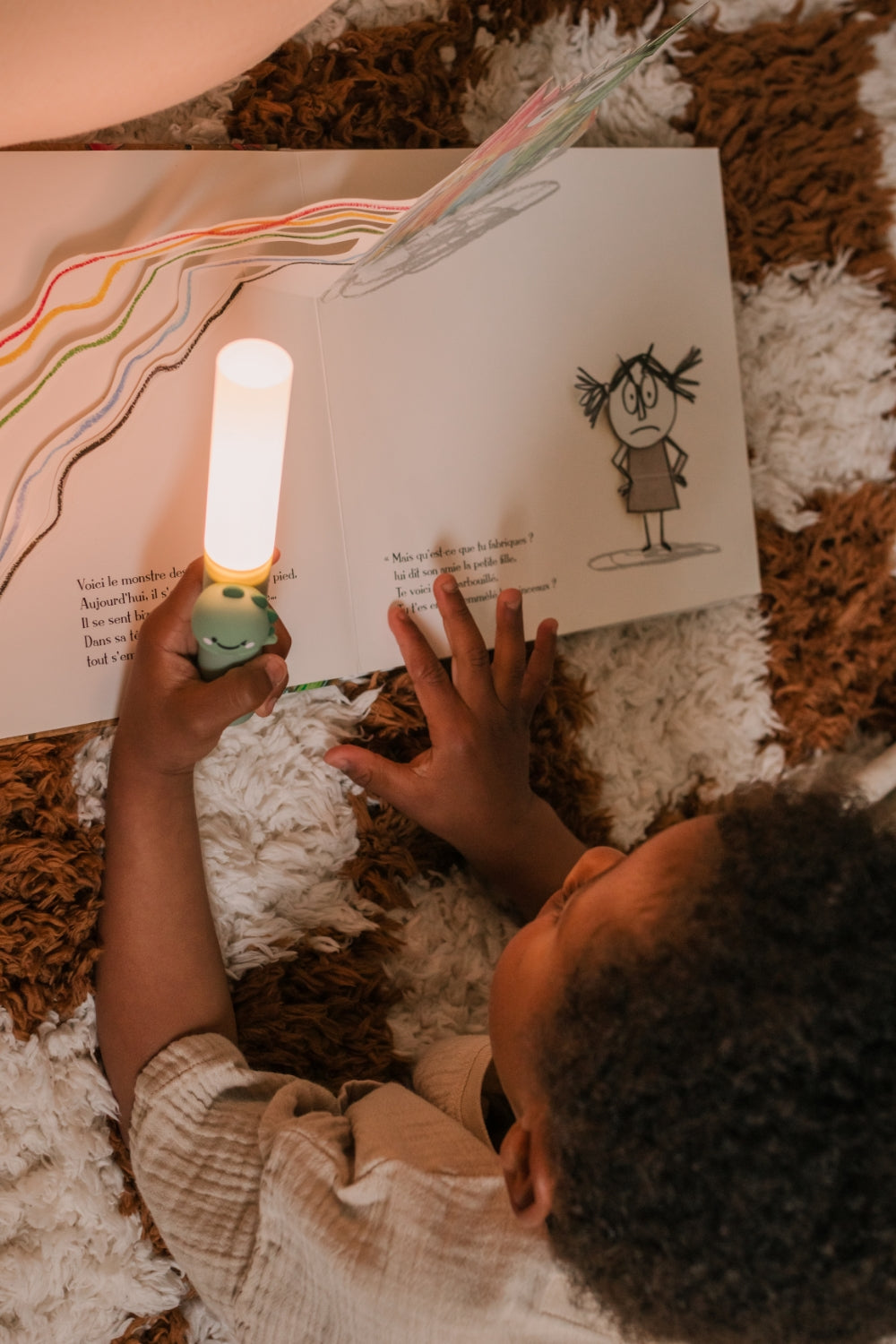 A child reading a book with a Zoo Light Dino on a textured surface.