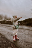 odaldino green silicon bag, child is carrying the bag around its neck, standing outside, pointing at a place, having a pair of binoculars in its hand