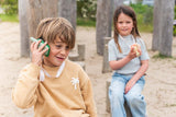 odalzoo walkie talkie set of dino green and pink, child is listening to the walkie talkie while other child is holding the walkie talkie, trees and tree trunks
