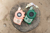 odalzoo walkie talkie set of dino green and pink, lying on a tree trunk