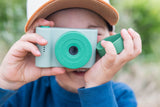 odalurban zoo dino green digital kids camera, child is taking a picture while holding the lenscover in its hands