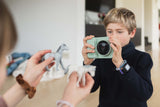 odalzoo print dino green digital kids camera, child is taking a picture of its friend who is holding animal toys