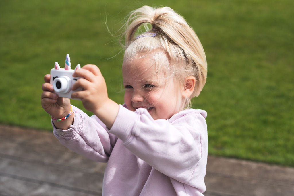 unicorn kids camera, child standing in garden, holding camera with both hands, laughing