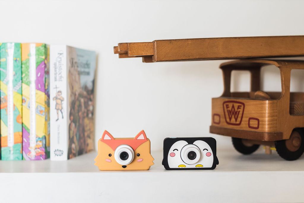 penguin and fox kids cameras, standing on cupboard next to childrens books and wooden fire truck