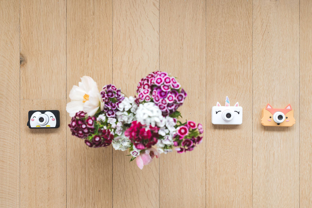 penguin, unicorn and fox kids cameras, lying next to flowers